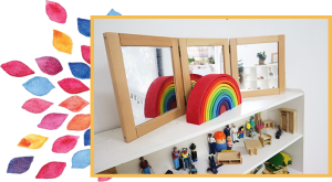 Shelves of wooden toys with wooden nesting rainbow and three mirrors on top shelf